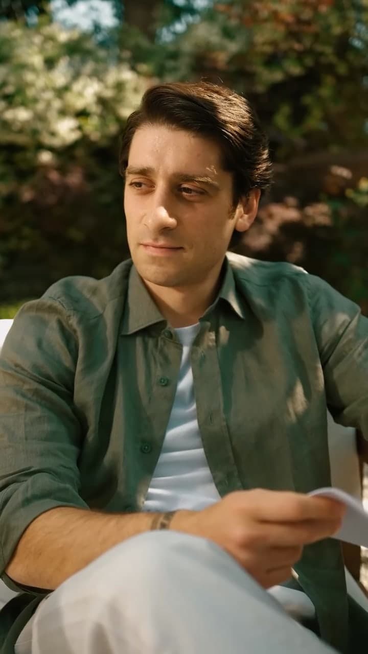 A man in a green linen shirt reading a card in a sunny garden.