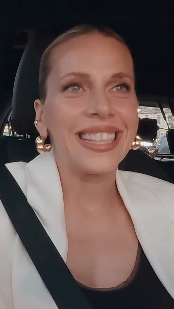 A woman in a white blazer smiling behind the wheel of a Mercedes-Benz.